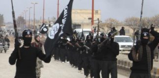 Origins of the Islamic State (ISIS): Who is Behind “Al Qaeda in Iraq”? Pentagon Acknowledges Fabricating a “Zarqawi Legend”/By Prof. Michel Chossudovsky A group of armed militants dressed in black uniforms holding flags.