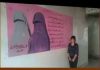 Western-supported Terrorist Diktats in Occupied areas of Syria/Photos by Reverend Ashdown/ June 2018 A woman stands beside a wall mural with Arabic text and an illustration of a veiled figure.