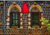 Holy Syria is Still Holy/By Rida Ali Stone wall with two windows decorated with plants and a large red pitcher.