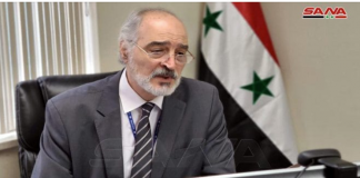 False Flag Anticipated By Syria’s permanent representative to the UN, Dr. Bashar al-Jaafari/ By Basma Qaddour A man with glasses and a beard speaking at a podium with Syrian flags behind him.