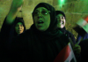 Aleppo, After Liberation/ By Prof. Anderson A group of women, one holding a flag, appearing passionate in a dimly lit setting.
