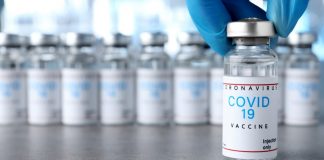 68-Year-Old Dies After Anaphylactic Reaction to COVID Vaccine as CDC Continues to Ignore Inquiry Into Increasing Number of Deaths/ By Megan Redshaw Close-up of a COVID-19 vaccine vial held by a gloved hand with more vials in the background.