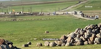 Inclusive Biden Junta Smuggles Additional 37 Oil Tankers Stolen from Syria/ By Arabi Souri Rural landscape with green fields, scattered rocks, and a distant convoy of vehicles.