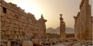 Apartheid Regime Bombs Syria in de facto Support for al Qaeda and ISIS/ By Seyed Marandi and Afshin Rattansi Ancient stone ruins with mountainous backdrop at sunset.
