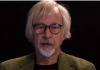 Dr. Wolfgang Wodard On The Dangers of Experimental Jabs An elderly man with white hair and glasses speaking against a dark background.