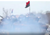 Ukrainian Armed Forces Openly Fly Flag of WW2 Nazi-Collaborating Banderite Fascists Protesters raising a red and black flag amid dense smoke.