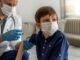 British Children Up to 52 Times More Likely to Die Following a COVID Shot: Government Report A young boy wearing a mask receives a vaccination from a healthcare worker.