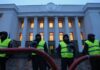 Opposition political parties banned in Ukraine and ‘unified information policy’ imposed/By Abdul Rahman Two security guards in yellow vests stand outside a lit building at dusk.