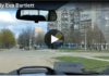 Streets of Mariupol/ By Eva Bartlett View from a car dashboard of an urban street with tall apartment buildings.
