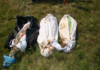 Russia’s Investigation into the Crimes Against the People of Donbass/By Investigative Committee of Russia Three wrapped bodies laid on grass, partially covered with black and white sheets.