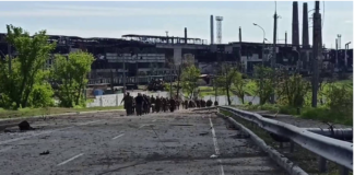 DOMINO EFFECT OF THE SURRENDER OF UKRAINIAN SOLDIERS IN AZOVSTAL ON THE REST OF UKRAINIAN TROOPS IN DONBASS/By Christelle Néant Group walking on a damaged road in an industrial area.