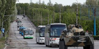 MARIOUPOL – REDDITION DES SOLDATS UKRAINIENS RETRANCHÉS DANS AZOVSTAL/ PAR Christelle Néant Military convoy including armored vehicle and buses on a road.