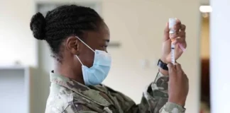 Video: US Military Oversaw Secret Contents of COVID Jabs/By Sasha Latypova, Dr. Sam Dube, Lara Logan, and et al. A soldier in uniform prepares a syringe while wearing a face mask.