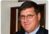 Russia Intercepts Nazi-Supporting Drone A man wearing glasses and a suit smiling indoors.
