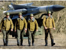 Soldiers walking in front of large missiles outdoors.
