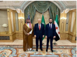 Three men in formal attire pose in an ornate room with flags in the background.