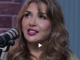 A woman speaking into a microphone with expressive makeup and styled hair.