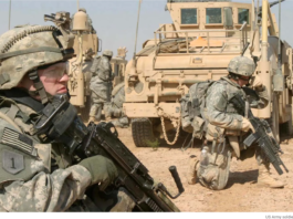 Soldiers resting near military vehicles in a desert setting.