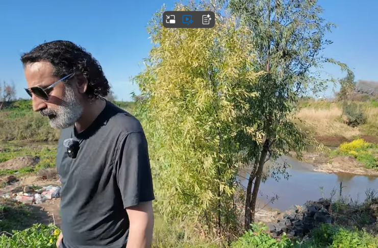 Man standing near a tree by a river on a sunny day.