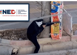 Masked shooter aiming rifle behind street crates