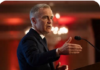 The Great Betrayal Man in suit speaking and gesturing at podium